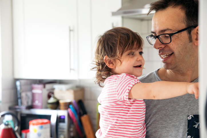 A father smiling as his daughter points to what treat she would like from the fridge. Daughter in the arms of her daddy.