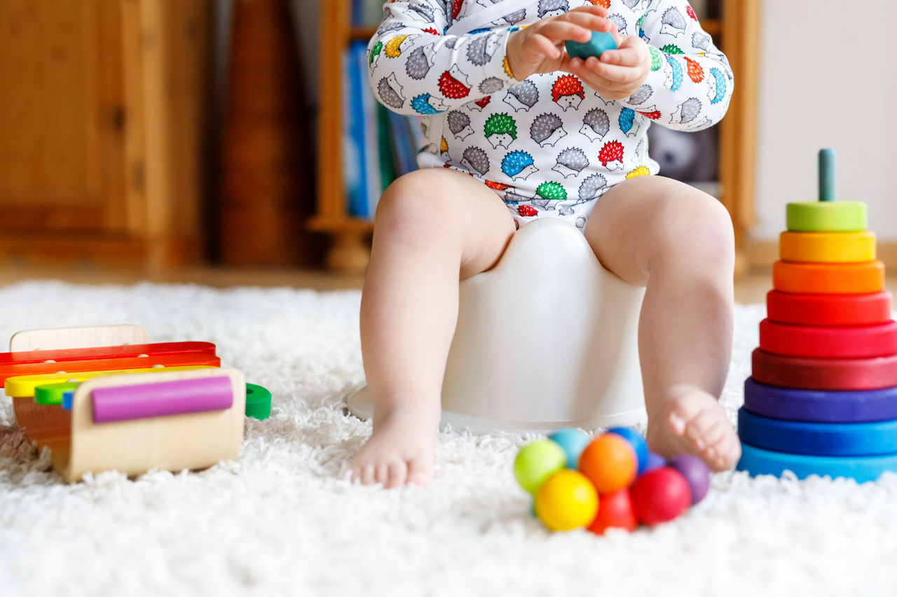 Closeup of cute little 12 months old toddler baby girl child sitting on potty. Kid playing with educational wooden toy. Toilet training concept. Baby learning, development steps.