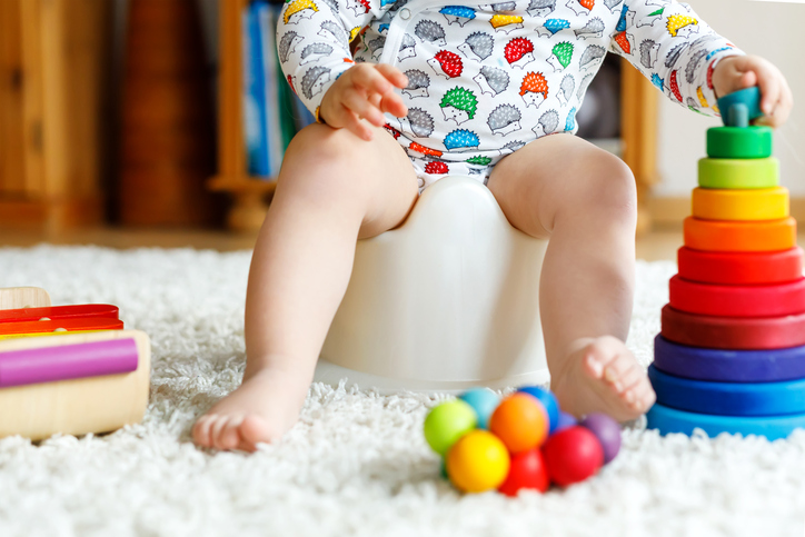 Closeup of cute little 12 months old toddler baby girl child sitting on potty. Kid playing with educational wooden toy. Toilet training concept. Baby learning, development steps.