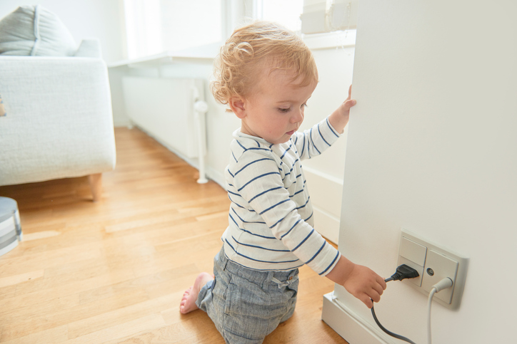 Scandinavian Danish bright interior with baby boy looking at electrical plug in the wall. The boy is tempted to play with the equiepment