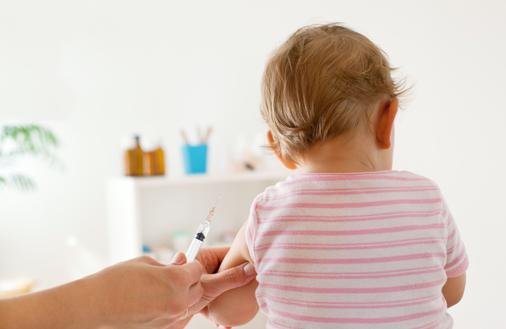 Bck View of baby girl patient receiving vaccine at the doctor's office, focus on hand holding vaccine