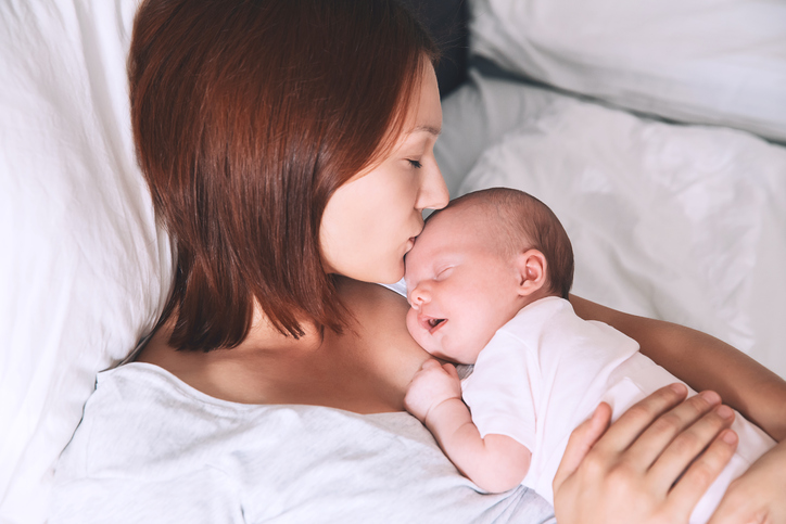 Mother kissing her newborn baby. Sleeping baby in the hands of his loving mother. Image of happy maternity and co-sleeping. Mom and child's first month of life at home.