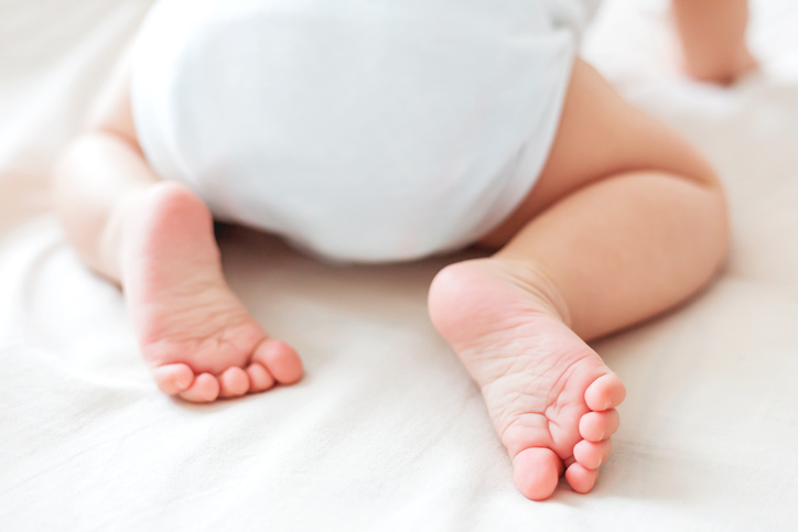 Baby's feet. Little child wearing white bodysuit and diaper. Cozy morning bedtime at home.
